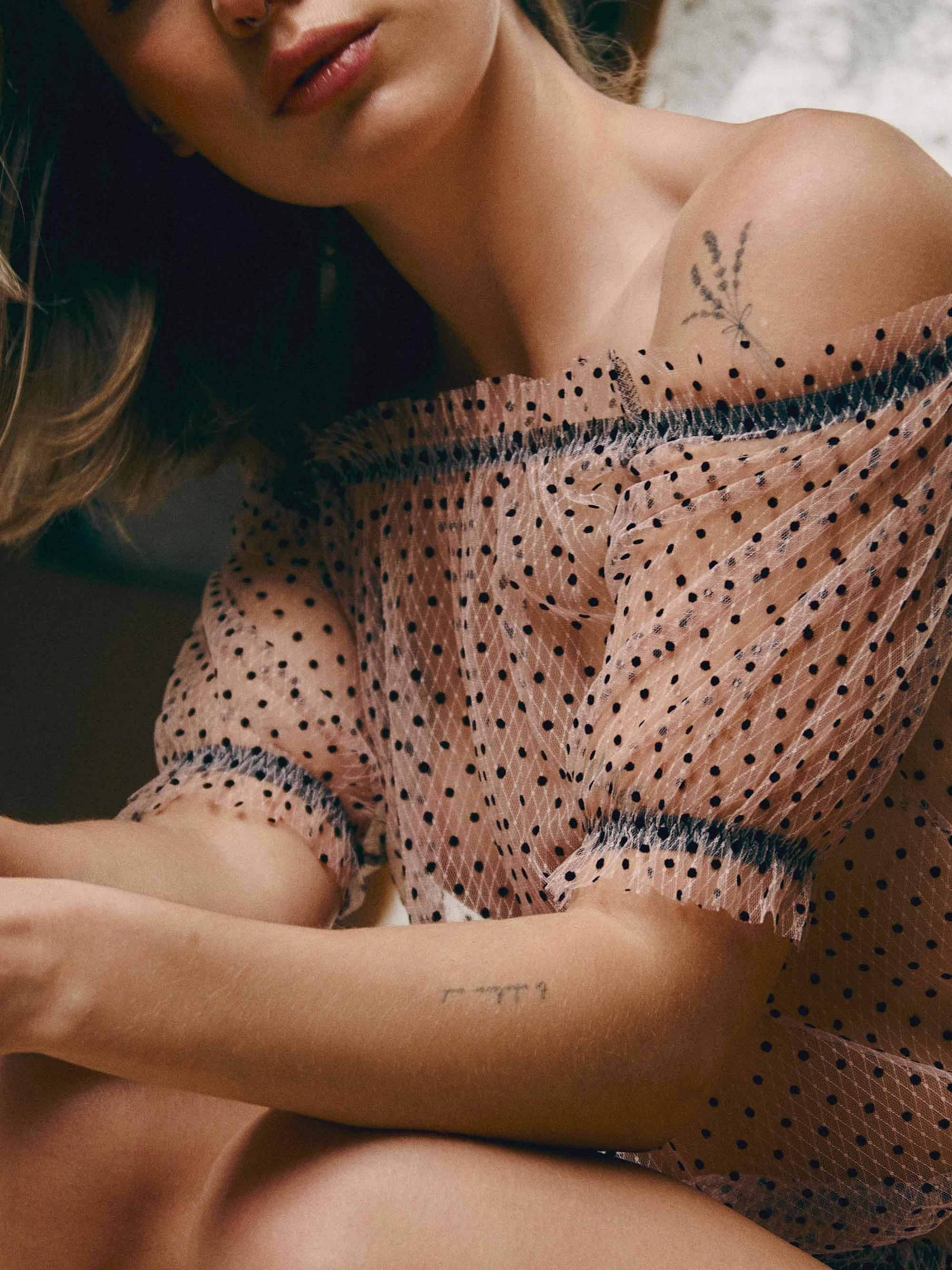 Frau in transparentem, gepunktetem Tüll-Oberteil mit Tattoo auf der Schulter, Nahaufnahme
