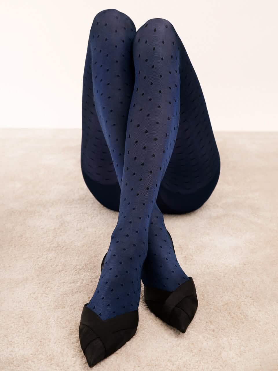 Blaue Strumpfhose mit Punkten, elegant kombiniert mit schwarzen Absatzschuhen auf Teppichboden.