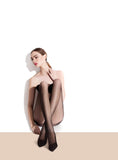 Frau trägt transparente schwarze Strumpfhose, sitzt elegant vor hellem Hintergrund